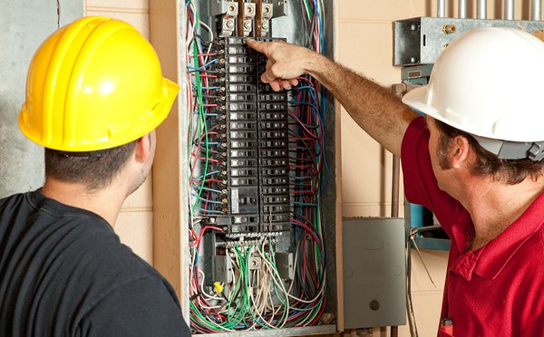 Two workers with hardhats looking at an electrical panel.
